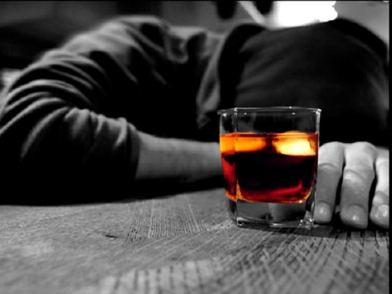 Человек лежит рядом со стаканом алкоголя